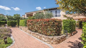 A pathway leading to a building with a stone wall and a hedge.