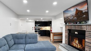 A modern living room with a sectional sofa, a fireplace, and a kitchen in the background. - Newly Remodeled 1BR | Shuttle, Fireplace, Amenities in the Heart of Killington (Killington)