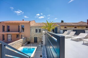 Un espace piscine agrémenté d’un mur en pierre, un bâtiment moderne avec un toit en tuiles et un bâtiment traditionnel doté d’une façade en pierre.