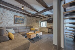 Un vaste espace de vie agrémenté d’un mur en pierre, de poutres en bois, d’un canapé, d’une table basse et d’un téléviseur.