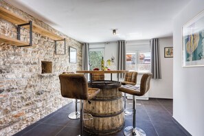 Un intérieur rustique avec un mur en pierre, un bar en forme de tonneau en bois, des tabourets de bar en cuir et une vue dégagée grâce à de grandes fenêtres.