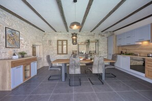 A modern kitchen with a stone wall, wooden beams, and grey chairs.