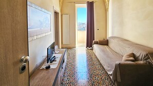 A room with a bed, a television, a patterned floor, a chandelier, and a view through an open door. - Sunday suite with private balcony (San Pancrazio Salentino)