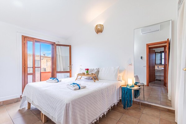 A hotel room with a bed, a bedside table, a lamp, a window with a view, and a door leading to the bathroom.