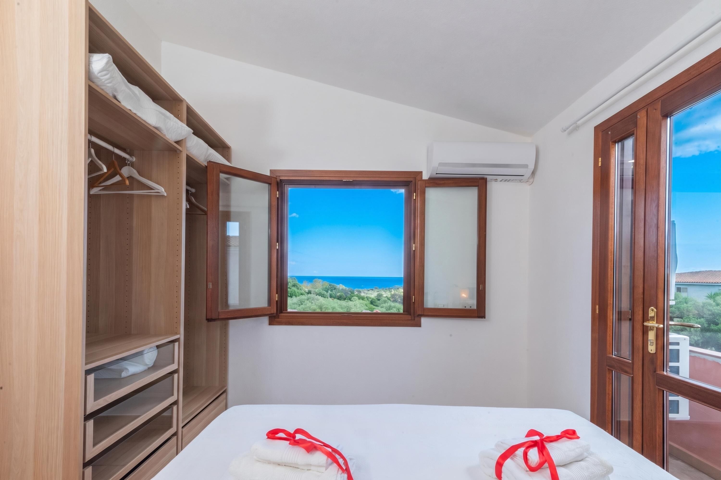 A hotel room with a bed, a wardrobe, a window with a view, and an air conditioning unit.