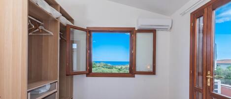 A hotel room with a bed, a wardrobe, a window with a view, and an air conditioning unit.