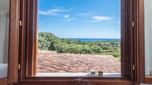 A wooden-framed window with a view of a terracotta-tiled roof and a cup and saucer on the windowsill.