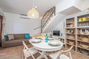 Uma área de refeições com mesa redonda, cadeiras, sofá, escada e estante.