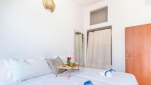 Een net opgemaakt bed met een blauwe handdoek, een houten nachtkastje met een bloemenvaas, en een gestreept kussen.