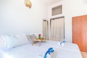 A neatly made bed with a blue towel, a wooden bedside table with a vase of flowers, and a striped pillow.