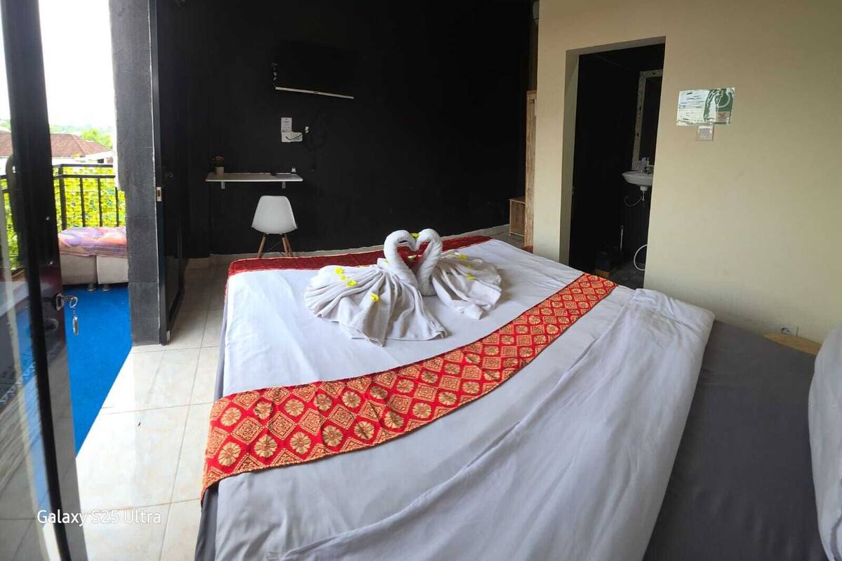 Ein Hotelzimmer mit Bett, einem kleinen Tisch, einem Sessel und Blick auf den Balkon.