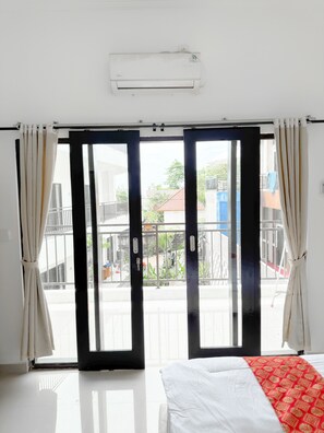 A hotel room with a bed, a sliding glass door to an outdoor balcony, and an air conditioning unit on the wall. - Ceria House Ungasan Uluwatu  (Ungasan)