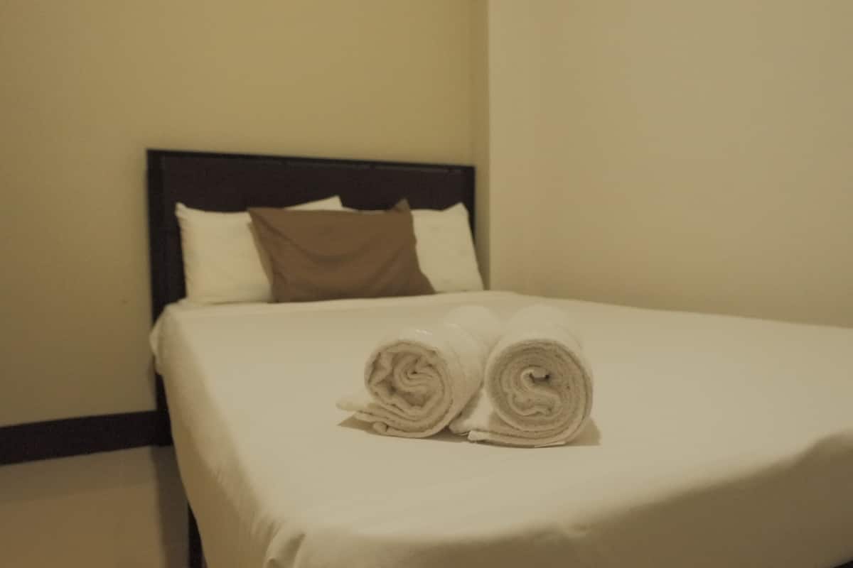 Een net opgemaakt bed met een witte dekbedovertrek en twee opgerolde handdoeken erboven.