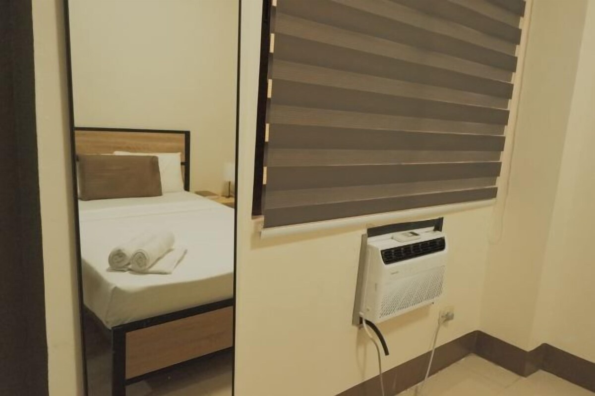 Un dormitorio con cama, mesita de noche, calentador de pared y ventana con persianas.