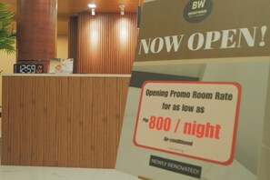 A hotel reception desk with a digital clock displaying 12:59 and a promotional sign for an opening promo room rate of 800 per night. - Brightwood Hotel & Residences (Manila)