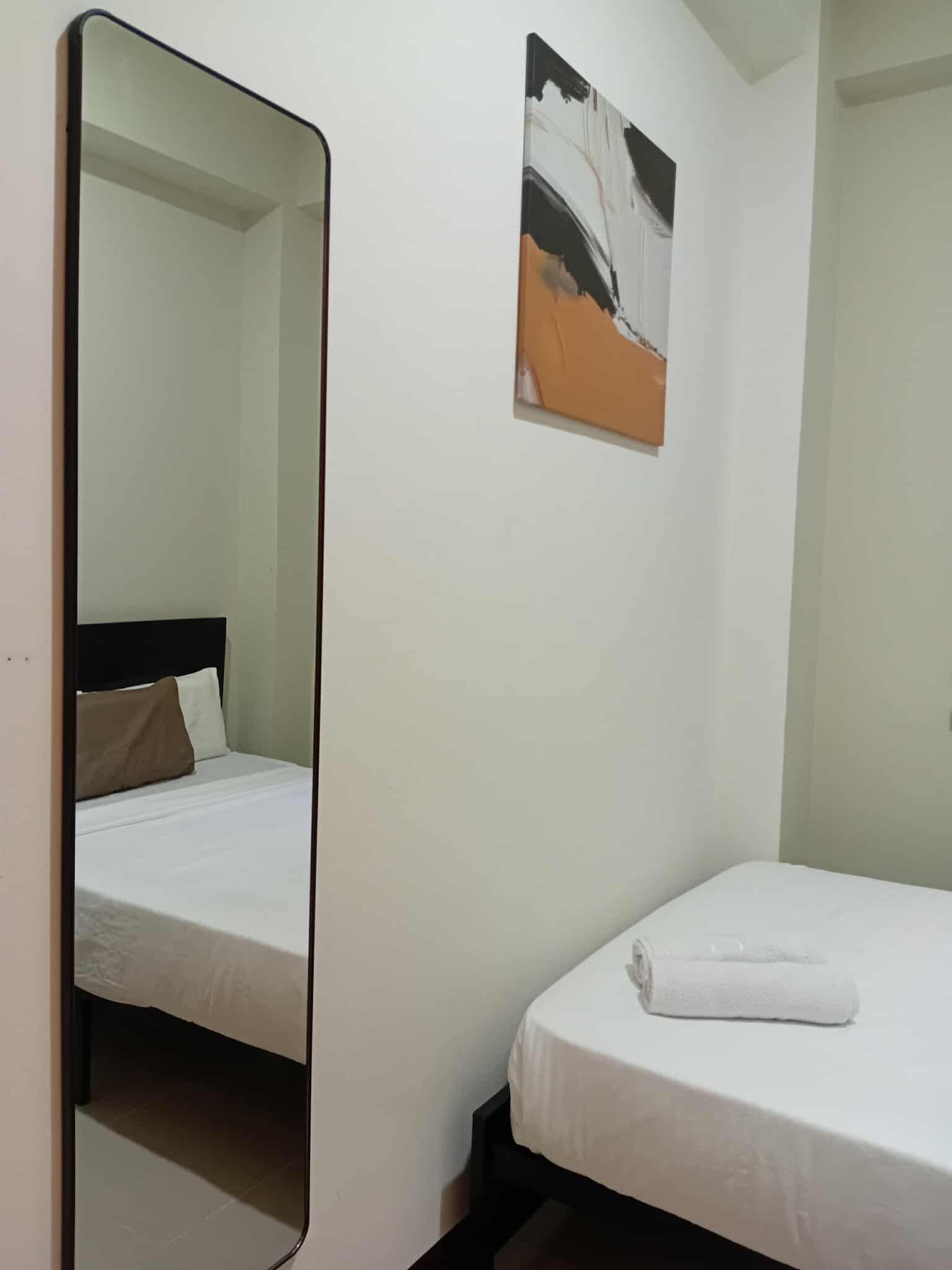 A bedroom with a bed, a bedside table, a mirror, and a painting on the wall.