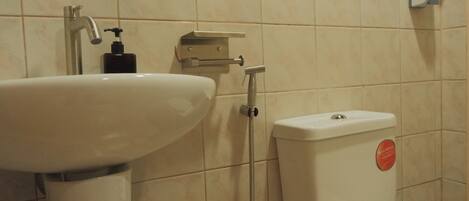 Un baño con lavamanos blanco, inodoro y cabezal de ducha de mano.