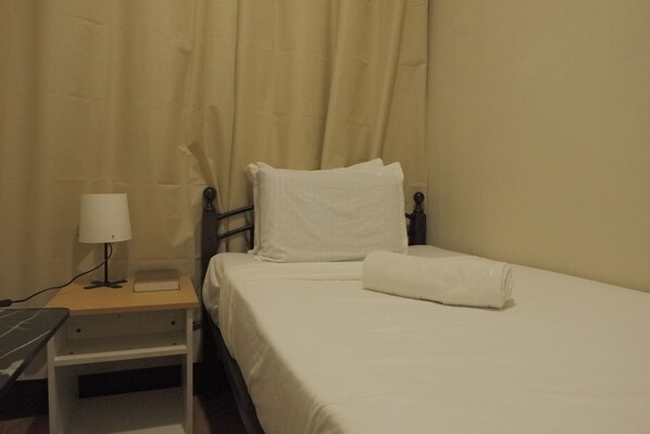 A neatly made bed with white linens, a bedside lamp, and a small bedside table with a book and a lamp. - Brightwood Hotel & Residences (Manila)