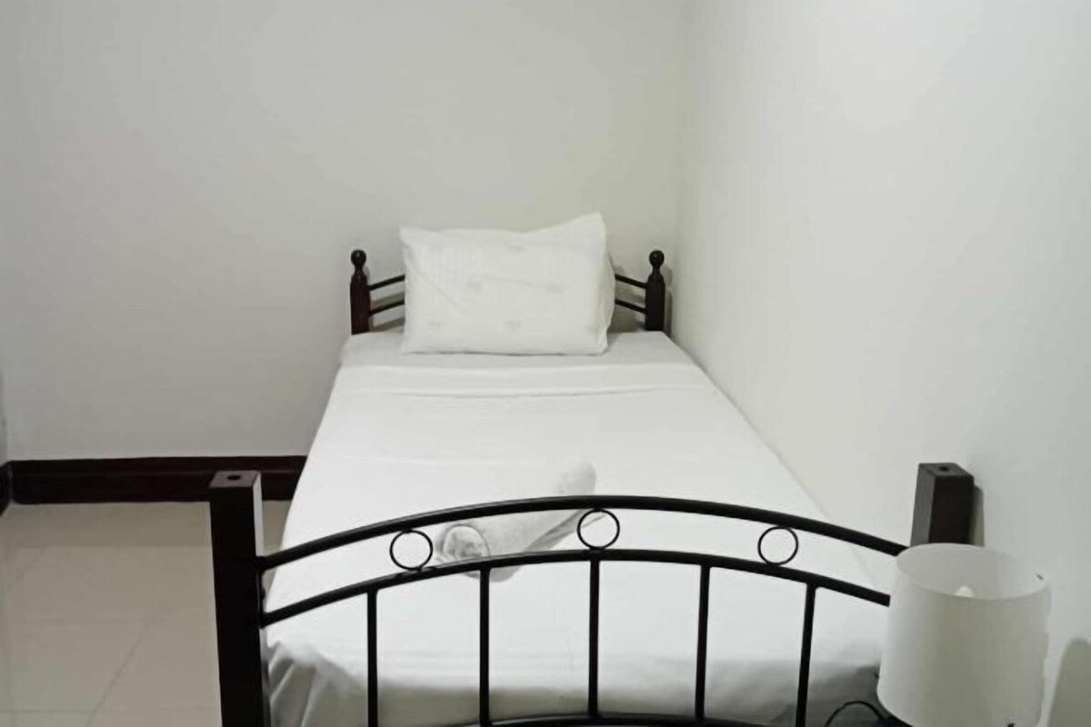 Una habitación pequeña con cama individual, cabecero de metal, colchón blanco y almohada blanca.