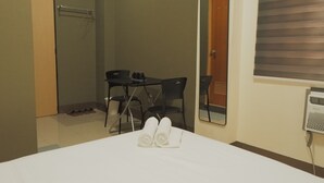 A hotel room with a bed, a small table with chairs, a shower, and a window with blinds. - Brightwood Hotel & Residences (Manila)