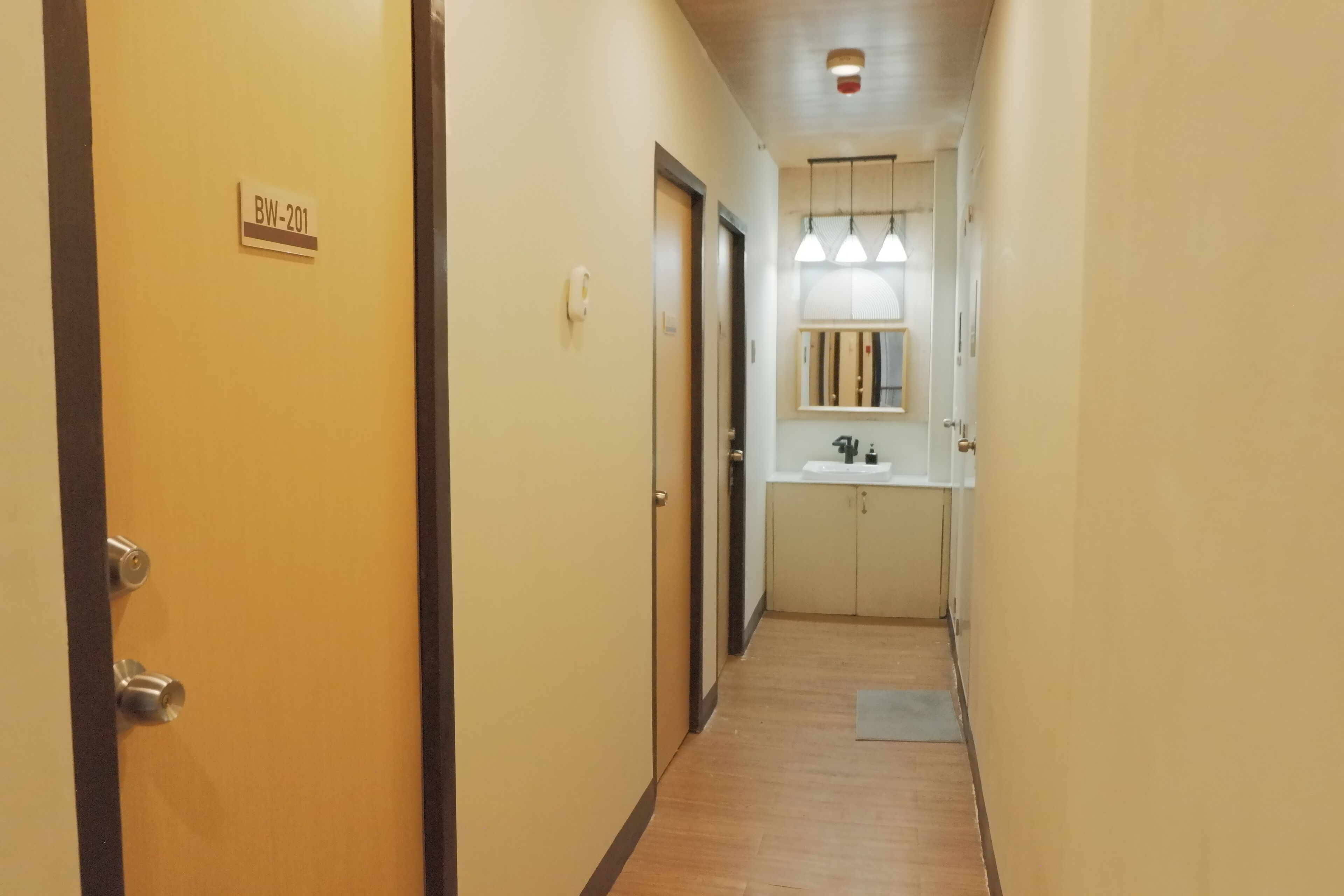 A narrow hallway with a wooden floor, a door labeled "BW-201", and a sink area with pendant lights.