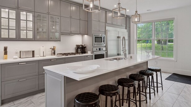 A modern kitchen with grey cabinets, stainless steel appliances, a large island with stools, and pendant lighting.