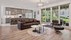 A modern kitchen with grey cabinets, a central island, and a dining area with a brown leather sofa and two round tables.