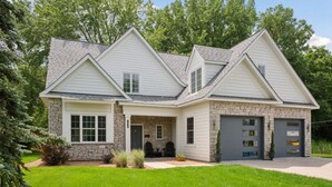 A two-story house with a stone facade, a garage, and a covered porch with outdoor seating.