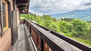 Ein hölzerner Balkon mit Blick auf grüne Hügel und Berge unter einem bewölkten Himmel.