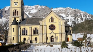 Eine Kirche mit einem Glockenturm und einem großen Rundfenster, umgeben von schneebedeckten Bergen.