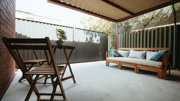 Relax in this serene outdoor seating area with a bench and chair, surrounded by lush greenery and a fence.