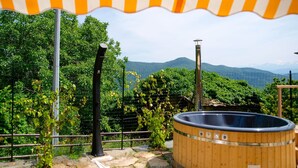 A wooden hot tub under a striped awning, surrounded by greenery and a mountainous backdrop. - Poderi Alugi Serravalle by Interhome (Piasco)