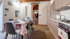 A modern kitchen with wooden beams, a dining area with a table set for four, and a view into a dining room. - Poderi Alugi Serravalle by Interhome (Piasco)