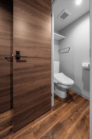A modern bathroom with a wooden floor, a white toilet, and a white wall.
