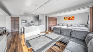Ett modernt hotellrum med ett litet kök, en soffa, en säng och ett stort fönster.