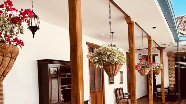 Un espacio al aire libre cubierto con pilares de madera, cestas de flores colgantes y suelo de baldosas.