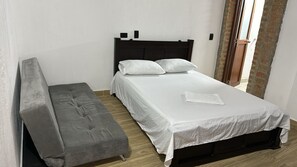 Un dormitorio con una cama, un banco gris y una colcha blanca.