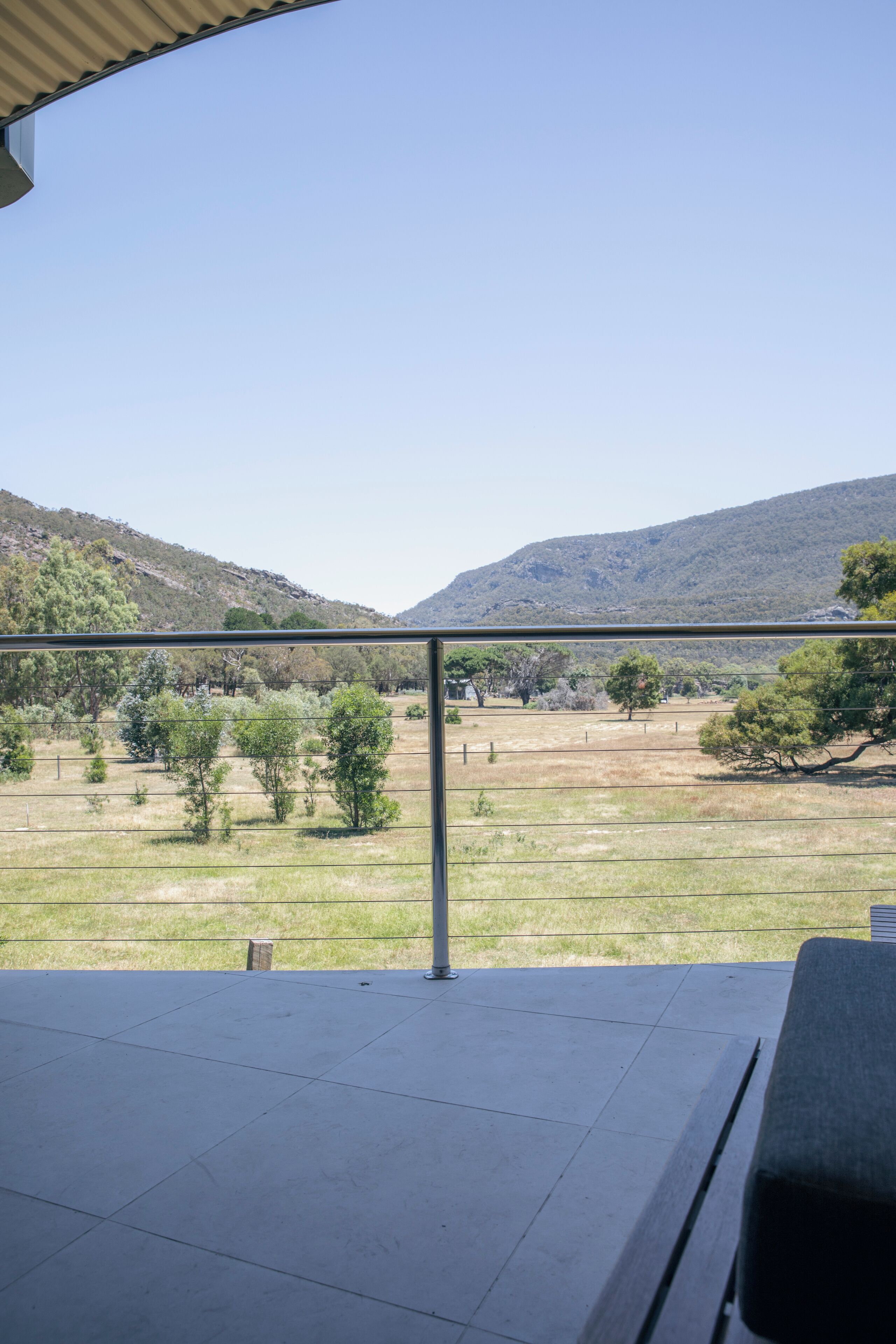 A balcony with a metal railing overlooking a grassy field and hills.