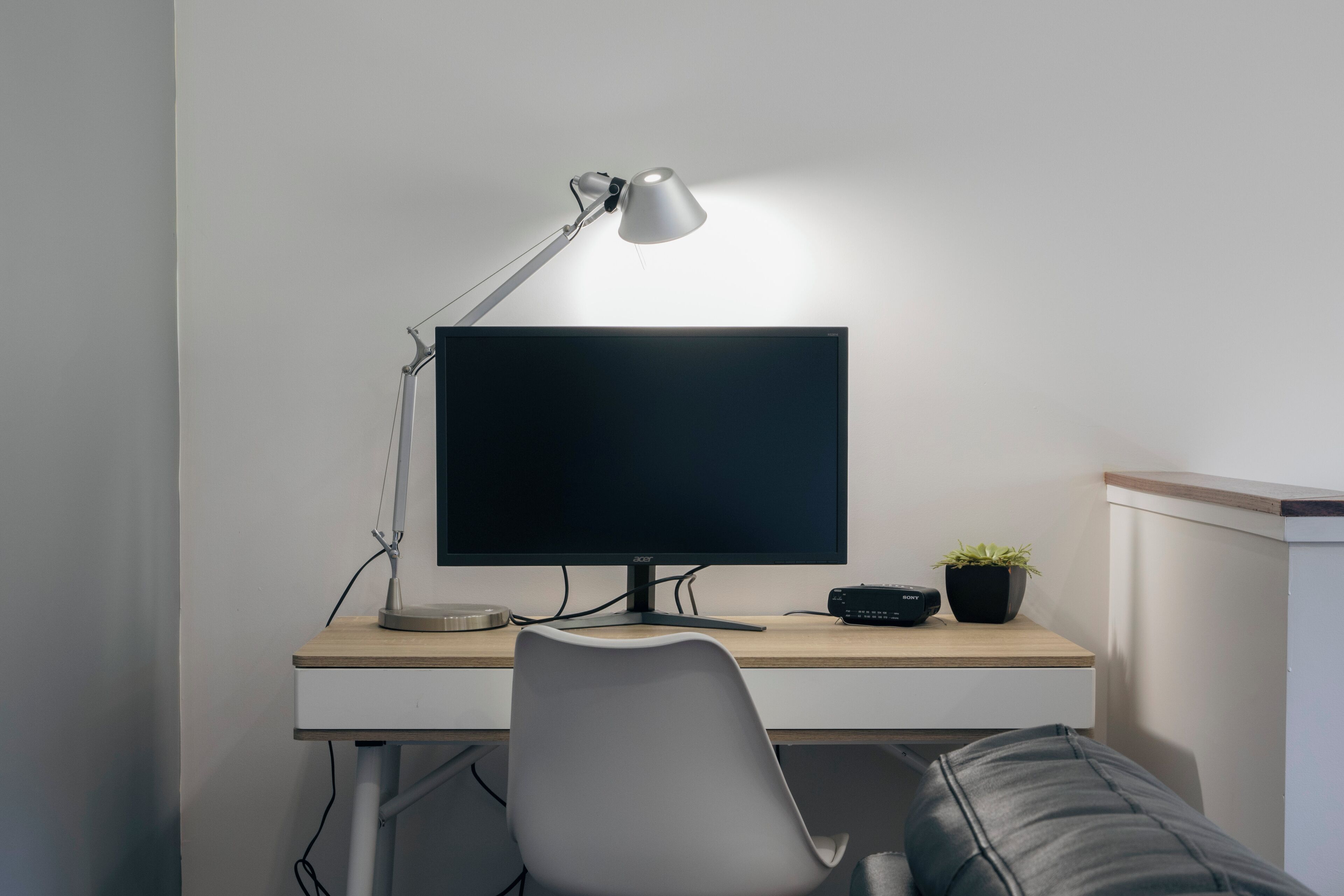 A modern workspace with a desk, a computer monitor, a desk lamp, a chair, a small plant, and a Sony speaker.