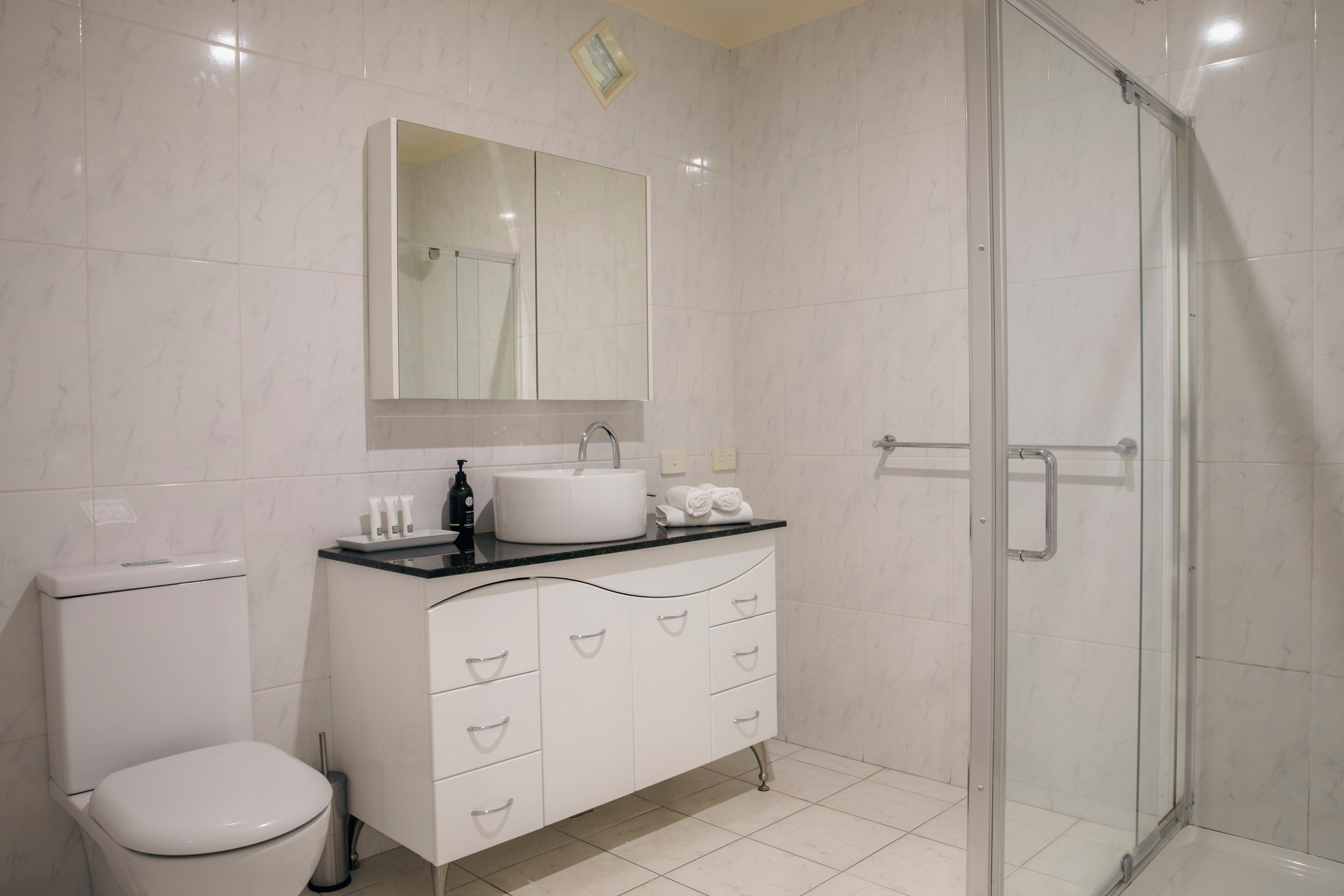 Ein modernes Badezimmer mit Toilette, Waschbecken, Waschtisch und einer Duschkabine aus Glas.