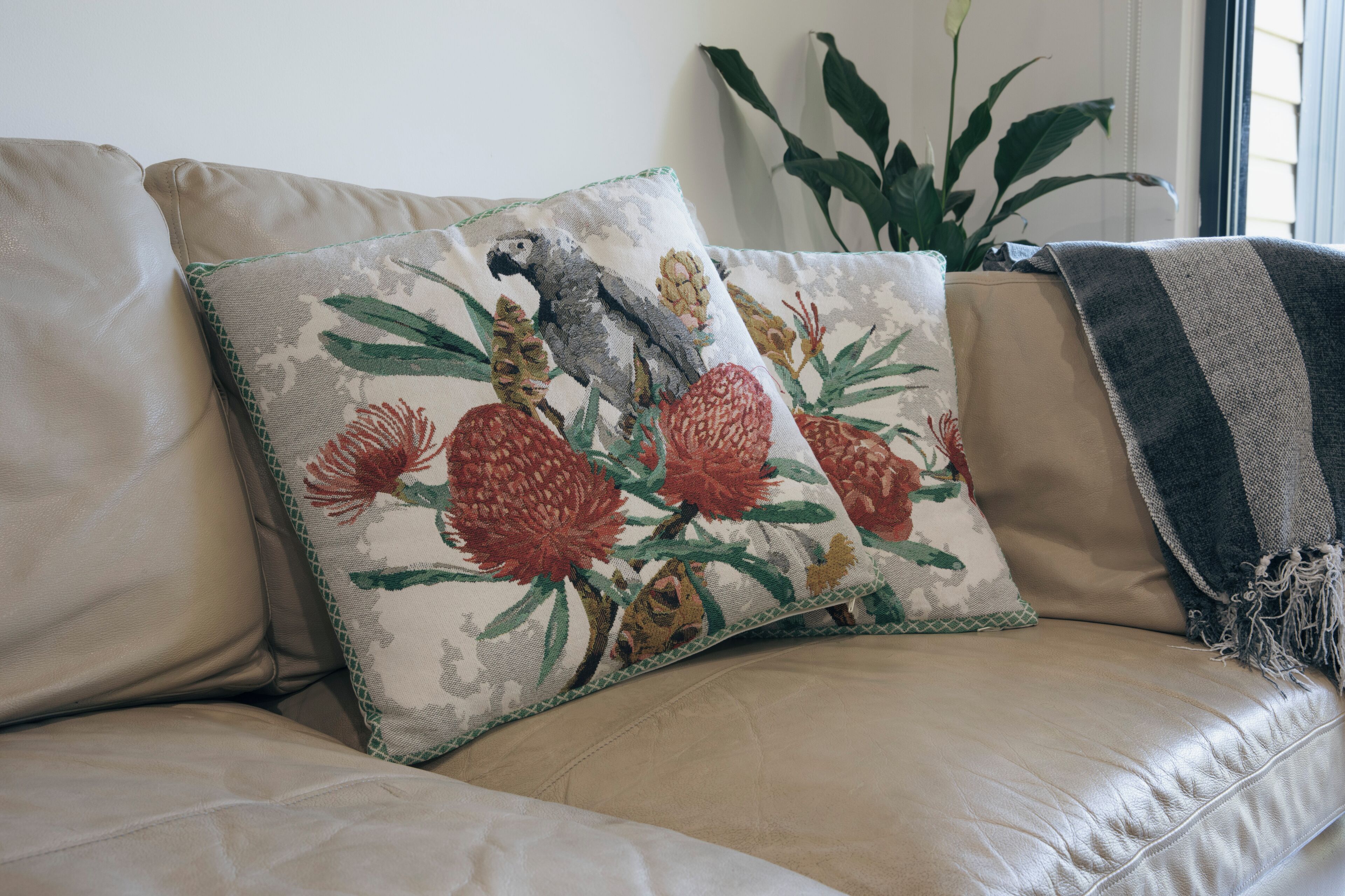 A beige leather sofa with a floral pillow featuring a bird and flowers.
