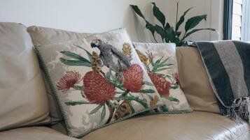 A beige leather sofa with a floral pillow featuring a bird and flowers.