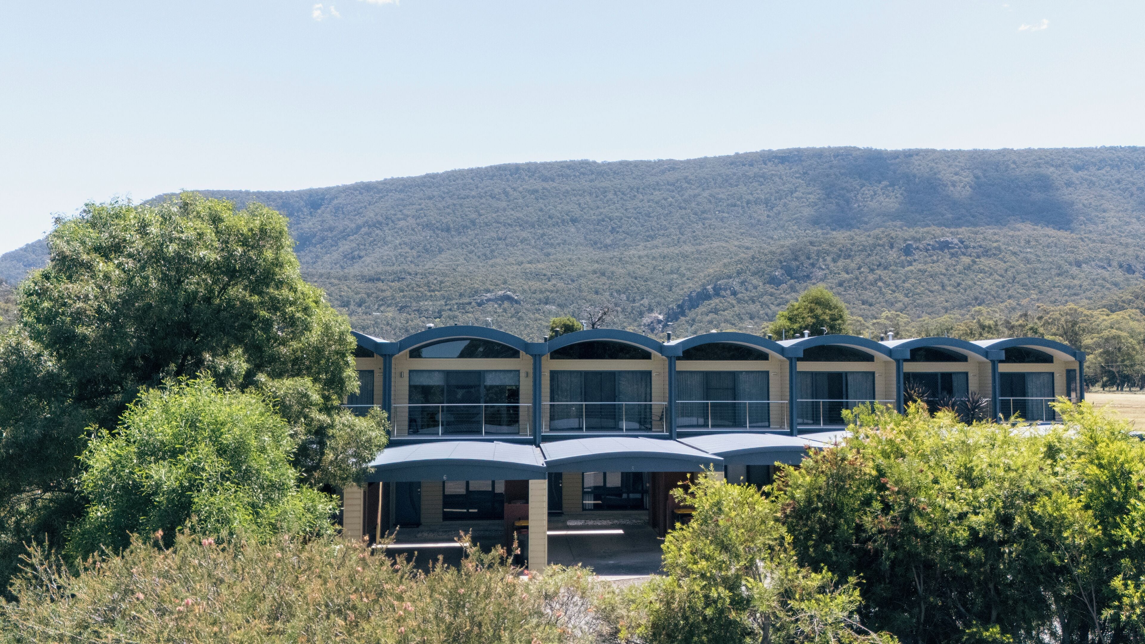 A modern building with a series of connected units, surrounded by lush greenery and a mountainous backdrop.