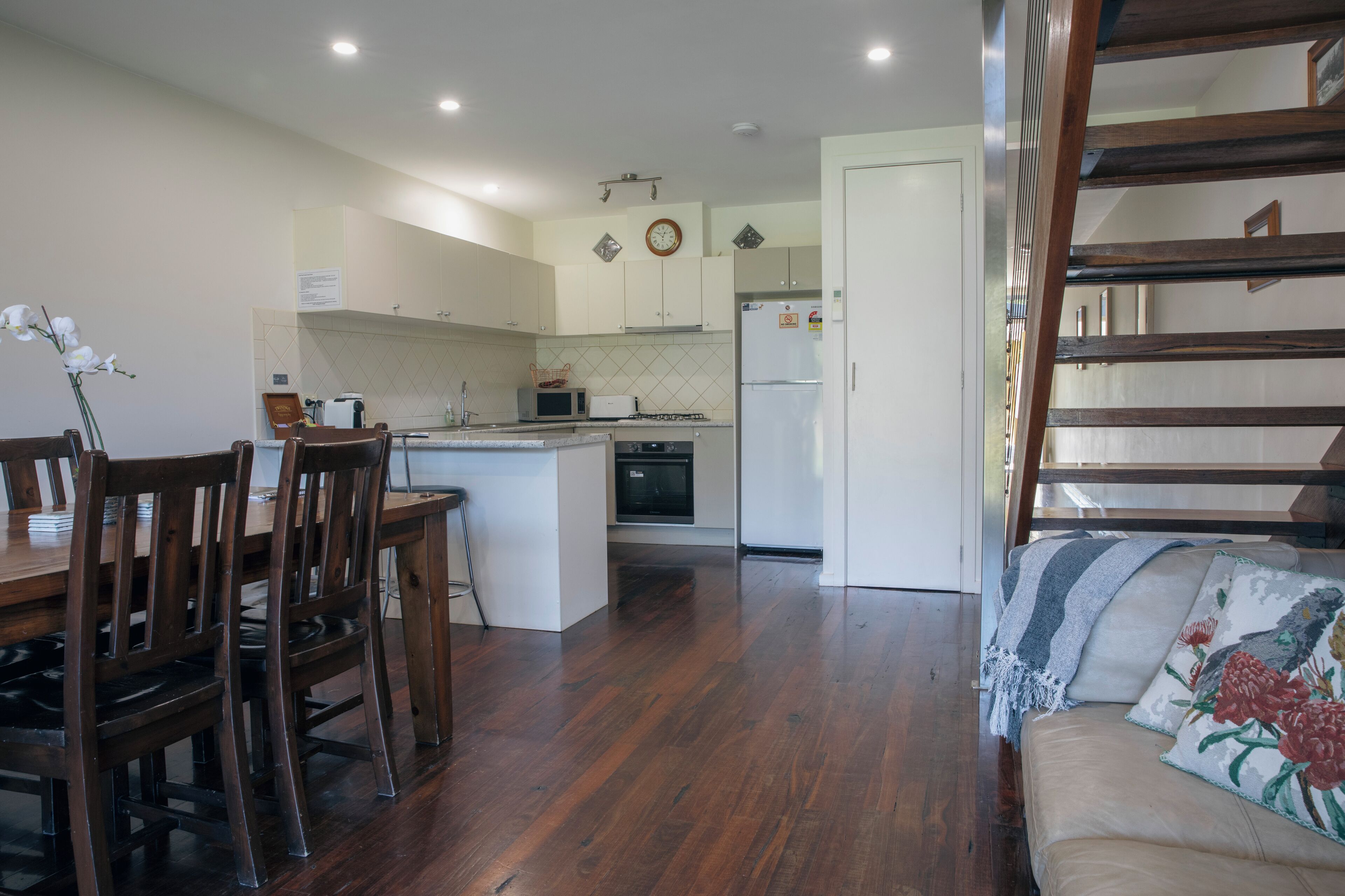 A kitchen with wooden cabinets, a microwave, and a refrigerator. There is a dining area with wooden chairs and a table.