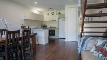 A kitchen with wooden cabinets, a microwave, and a refrigerator. There is a dining area with wooden chairs and a table.
