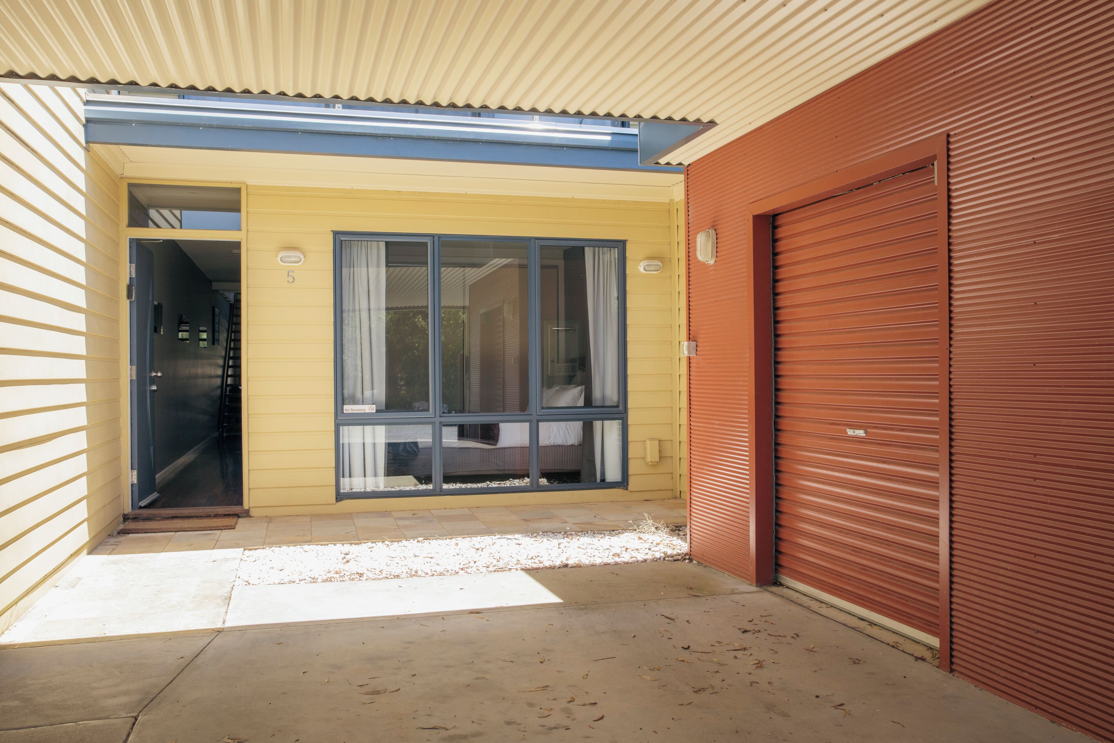 A building with a yellow exterior, a blue door, and a red garage door.