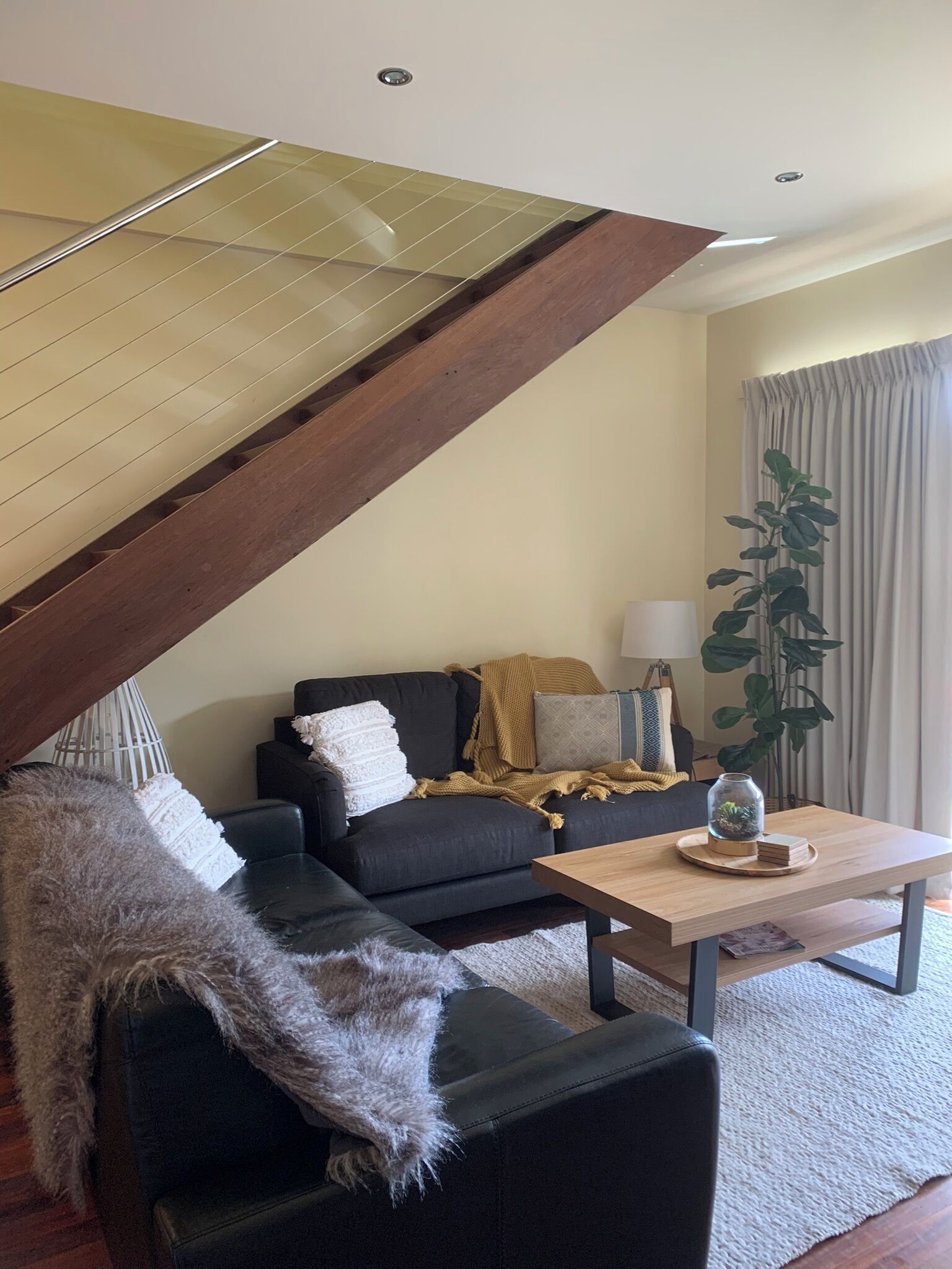 Sala moderna com um sofá preto, uma mesa de centro de madeira e uma escada com guarda-corrimão de vidro.