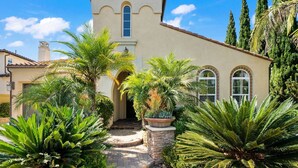 A Mediterranean-style building with a central entrance, surrounded by lush greenery and palm trees. - Spacious w/ Yard, BBQ, Presidio Access Near Park, Pool, Tennis, Beaches & Legoland! Extended Stays (Carlsbad)