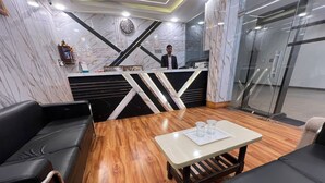 A modern reception area with marble walls, a reception desk, black leather seating, and a wooden floor. - Hotel Aero Fly (New Delhi)