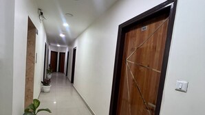 A long, narrow hallway with white walls and a tiled floor, leading to multiple doors. - Hotel Aero Fly (New Delhi)